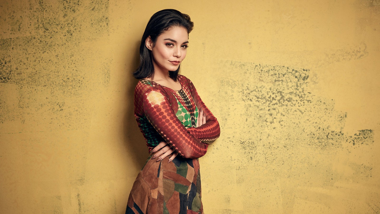 Femme dans une robe colorée s'appuyant contre un mur jaune (vanessa hudgens, théâtre musical, coiffure, épaule, humain)