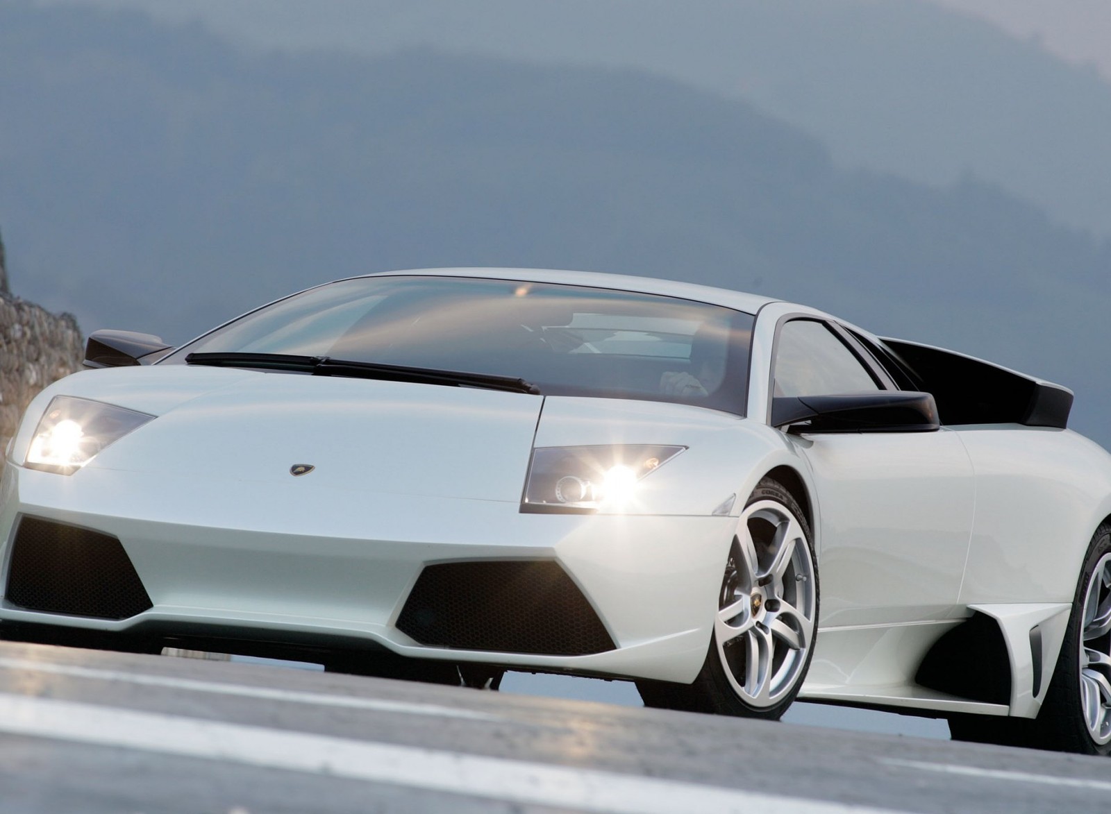 Um close de um carro esportivo branco dirigindo em uma estrada (lamborghini, white sports car)