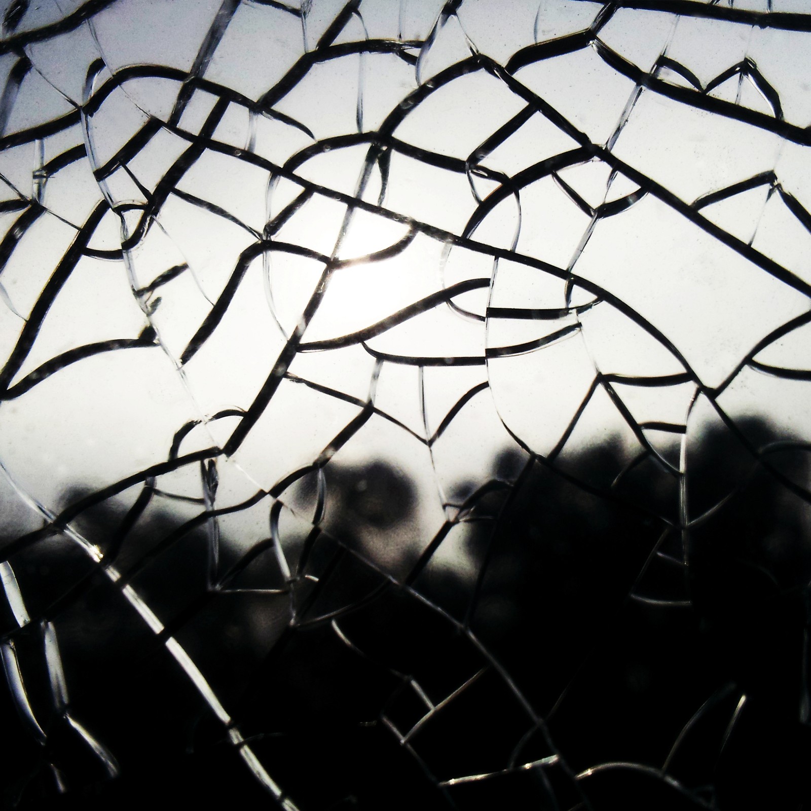 A close up of a broken glass window with a sun in the background (broken, glass)