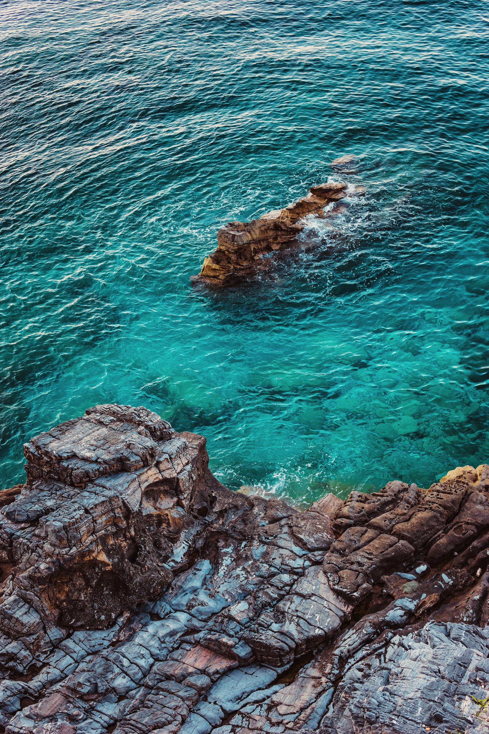 Uma pessoa está em pé sobre uma rocha olhando para o oceano (corpo de água, mar, água, costa, rocha)