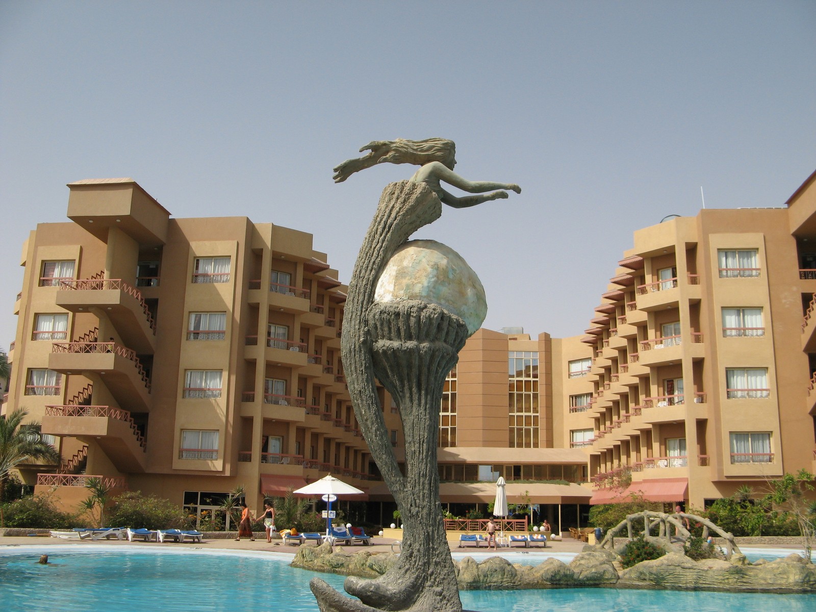 There is a statue of a woman riding a dolphin in a pool (architecture, building, apartment, facade, condominium)