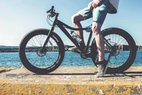 Bicicleta de montanha estacionada à beira-mar, com um ciclista descansando no quadro.