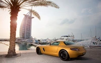 Golden Mercedes-Benz SLS AMG parked by the marina with Burj Al Arab in the background, surrounded by palm trees and yachts.