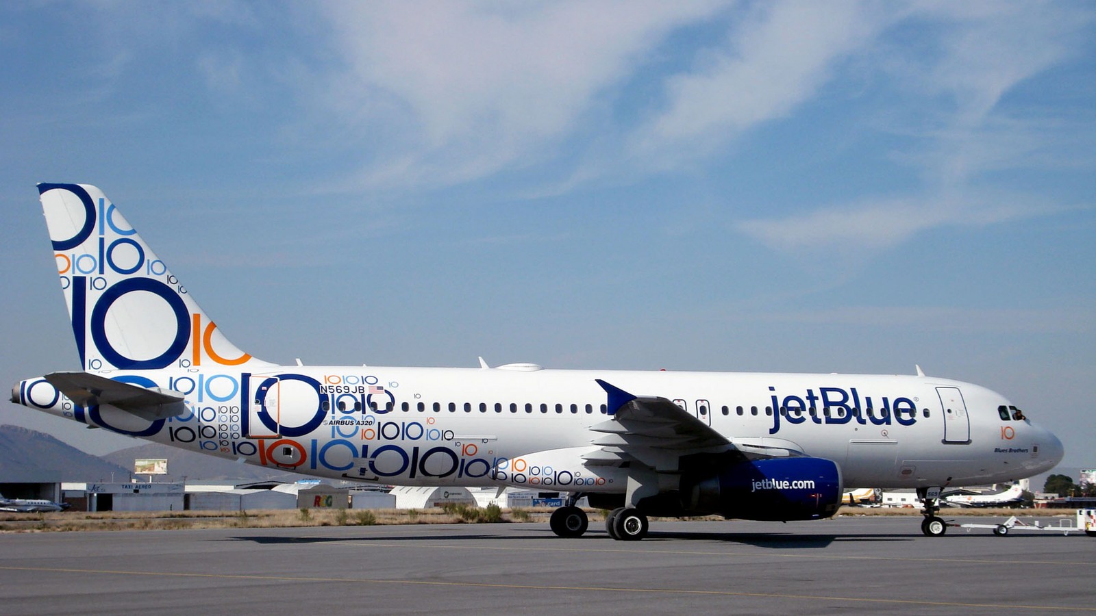 Um avião a jato pintado de azul na pista com montanhas ao fundo (linha aérea, voo, airbus, viagem aérea, aeronave comercial)