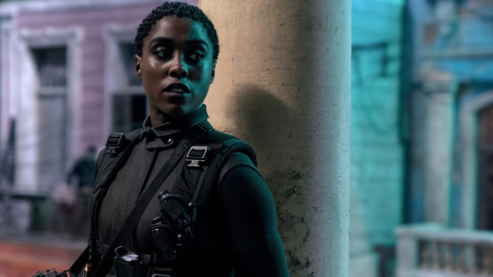 Un primer plano de una persona de pie junto a un edificio con un arma (no time to die, película, 2020, nomi, lashana lynch)