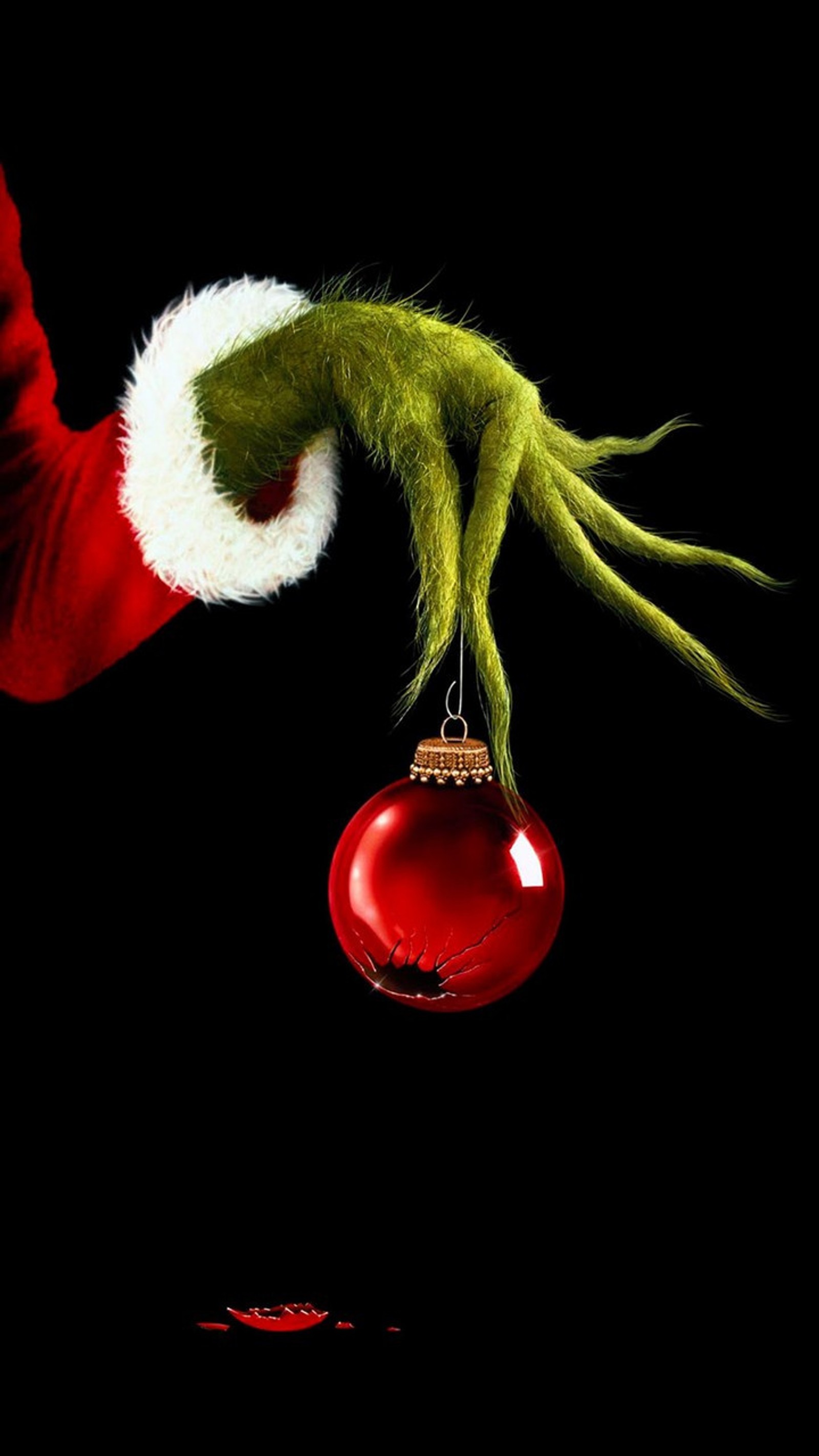 A close up of a person holding a red ornament with a green hand (grinch, christmas, stole, holiday, green)