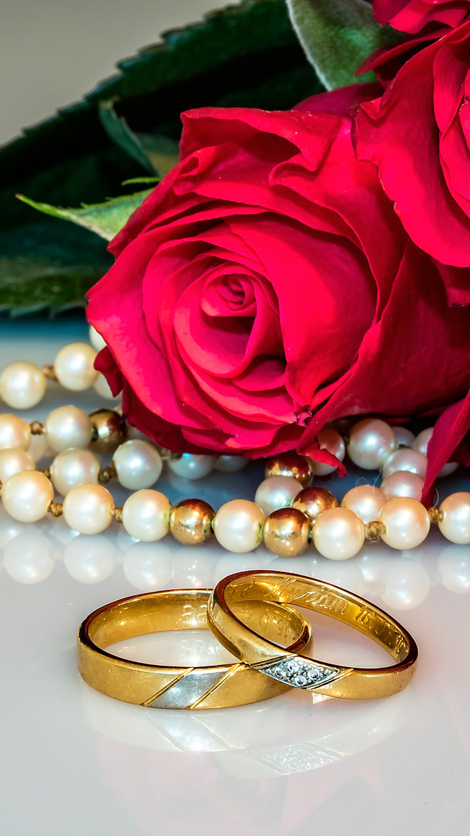 Dos anillos de boda y una rosa sobre una mesa con perlas (ramo, novia, flores, groom, feliz)