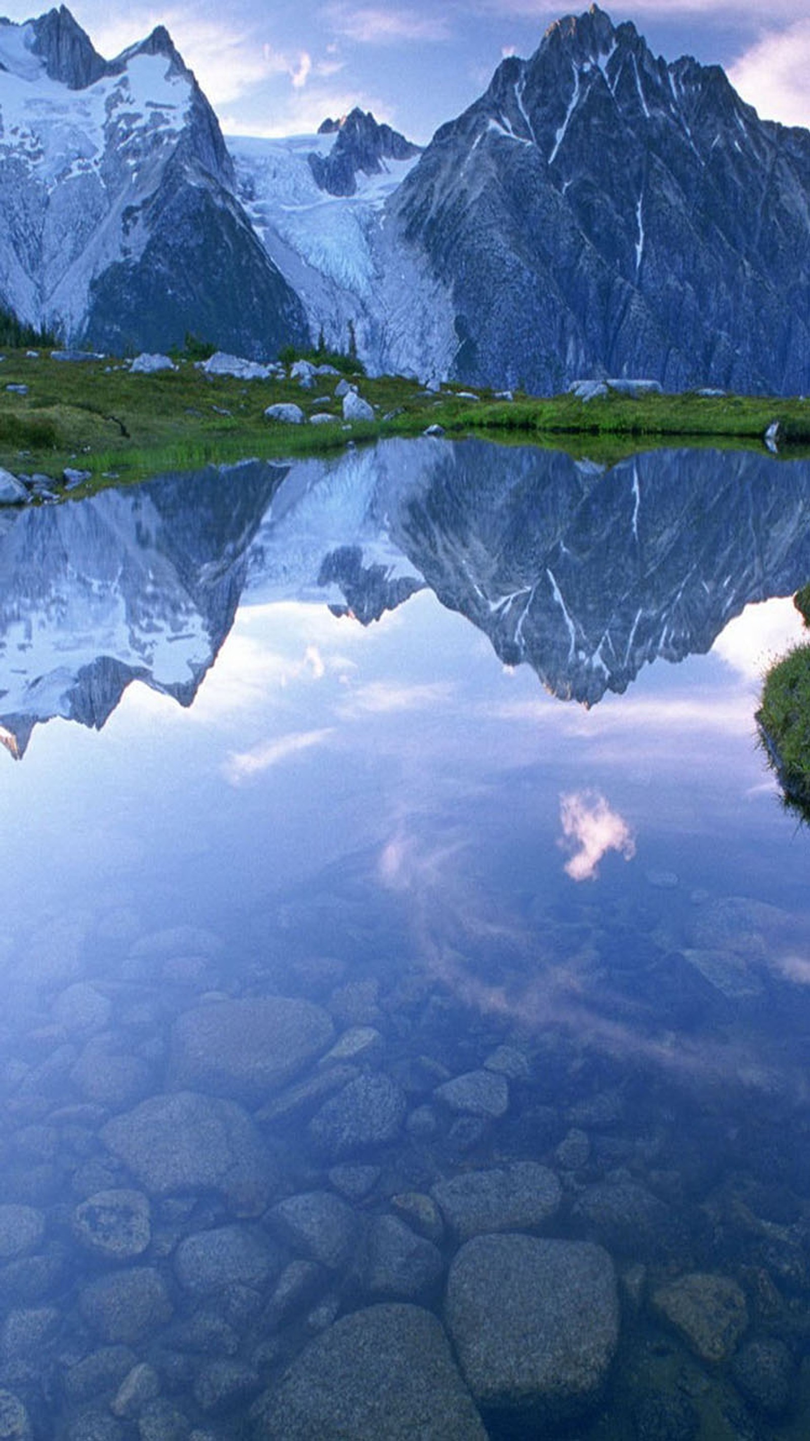 Montanhas refletidas em um lago com pedras e grama (lago, água)