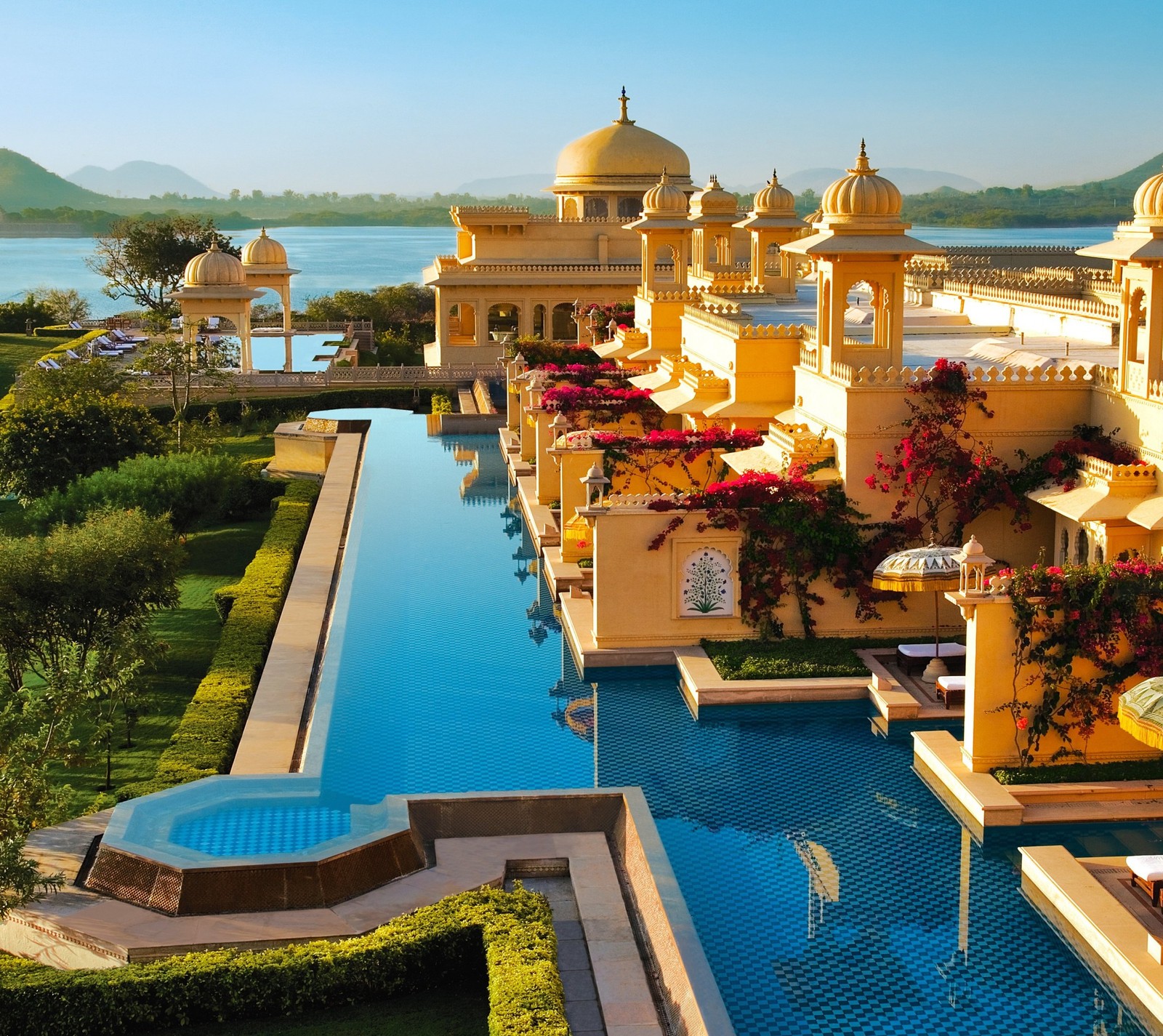 Vista aérea de uma piscina e um palácio com um lago ao fundo (hotel, índia, india, piscina, água)