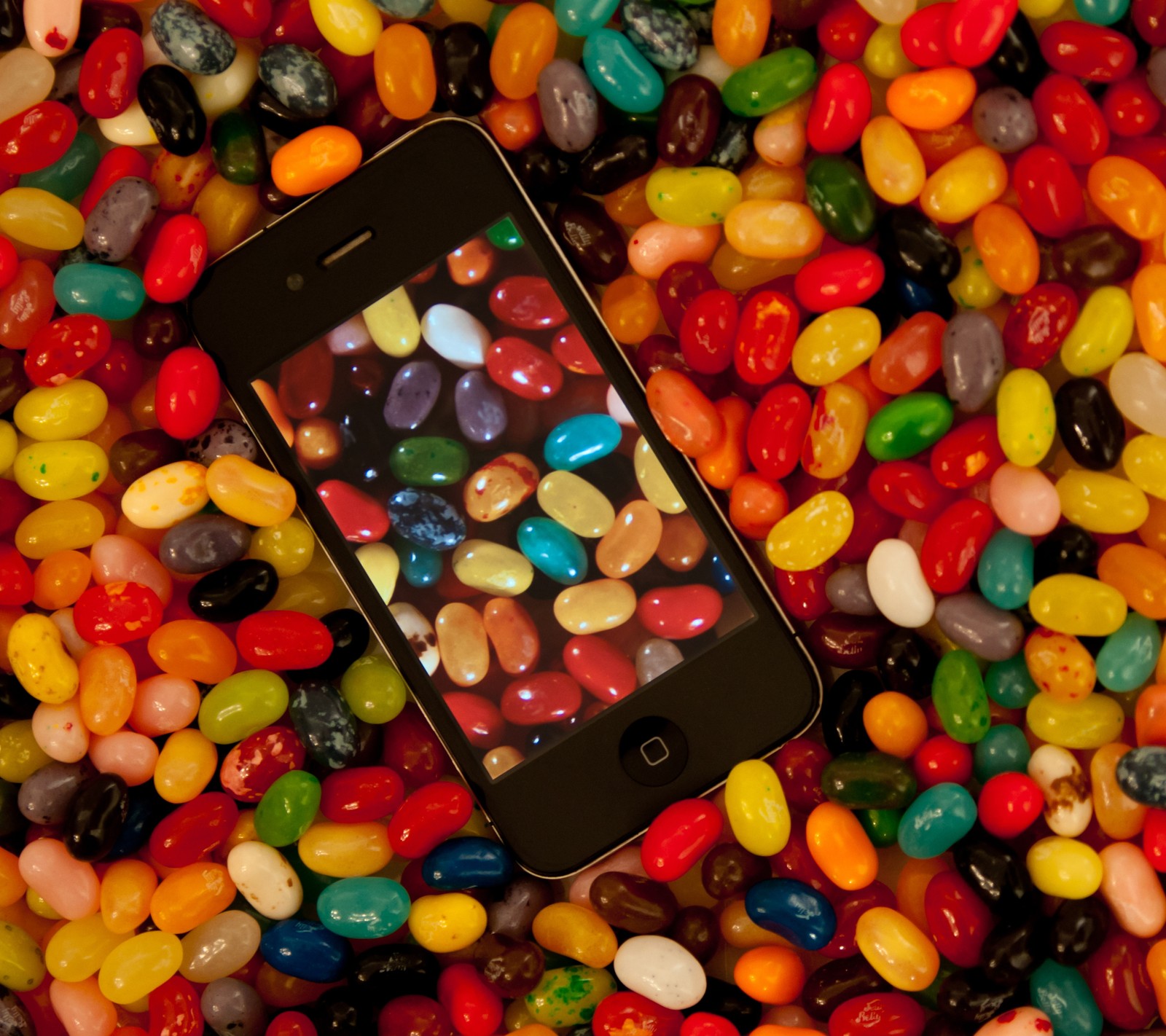 Un primer plano de un teléfono celular rodeado de jelly beans. (frijoles, dulces, colorido, comida, gelatina)