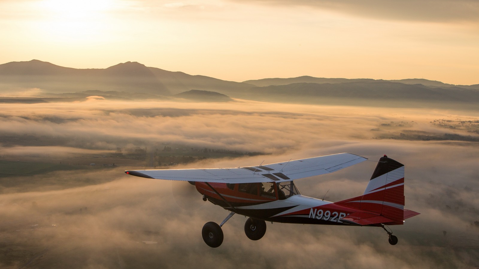 Um avião voando sobre um vale com uma montanha ao fundo (aeronave, voo, aviação, viagem aérea, aeronave leve)