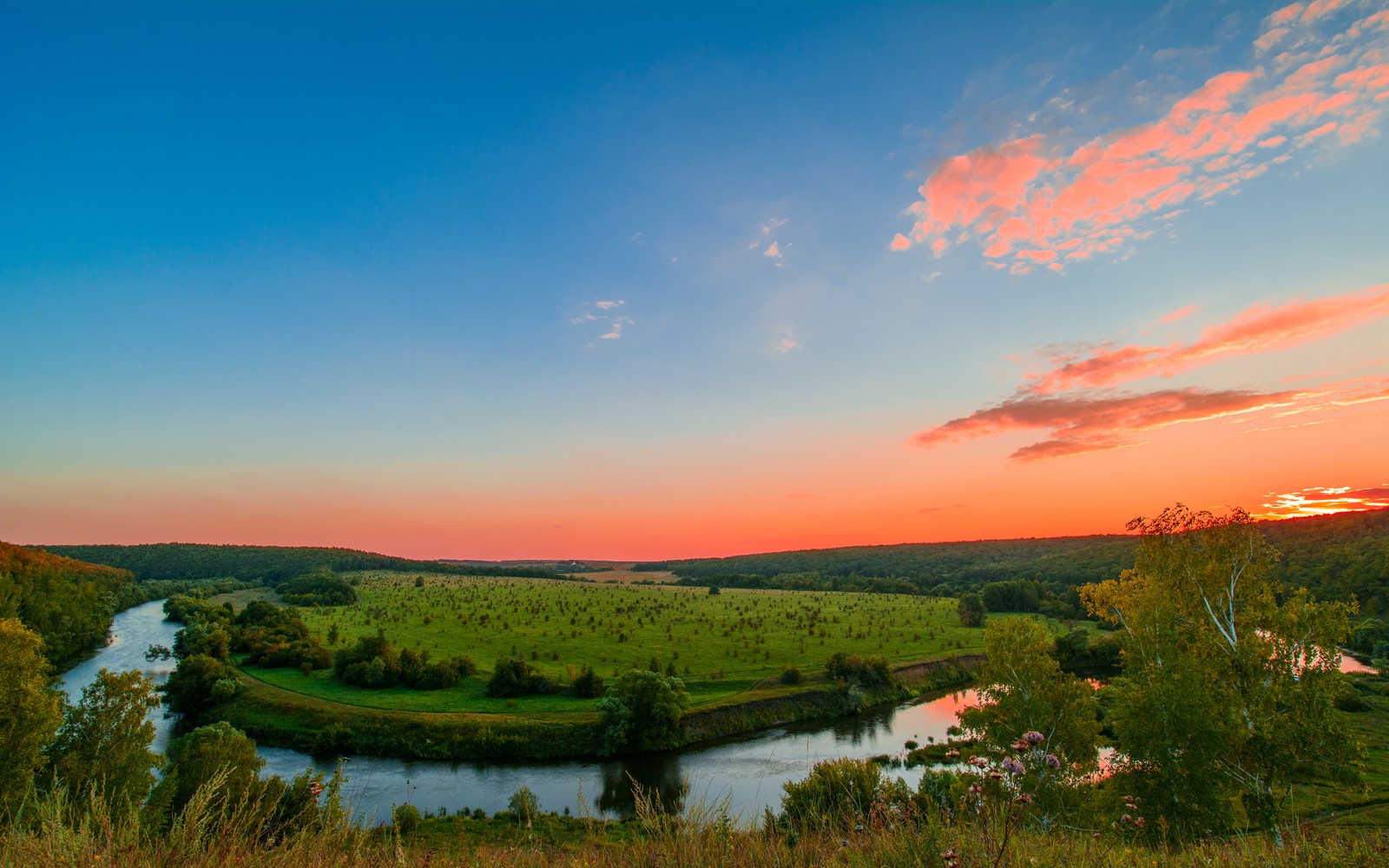 A view of a river running through a lush green field (upa river, tula region, russia, sunset orange, clear sky)