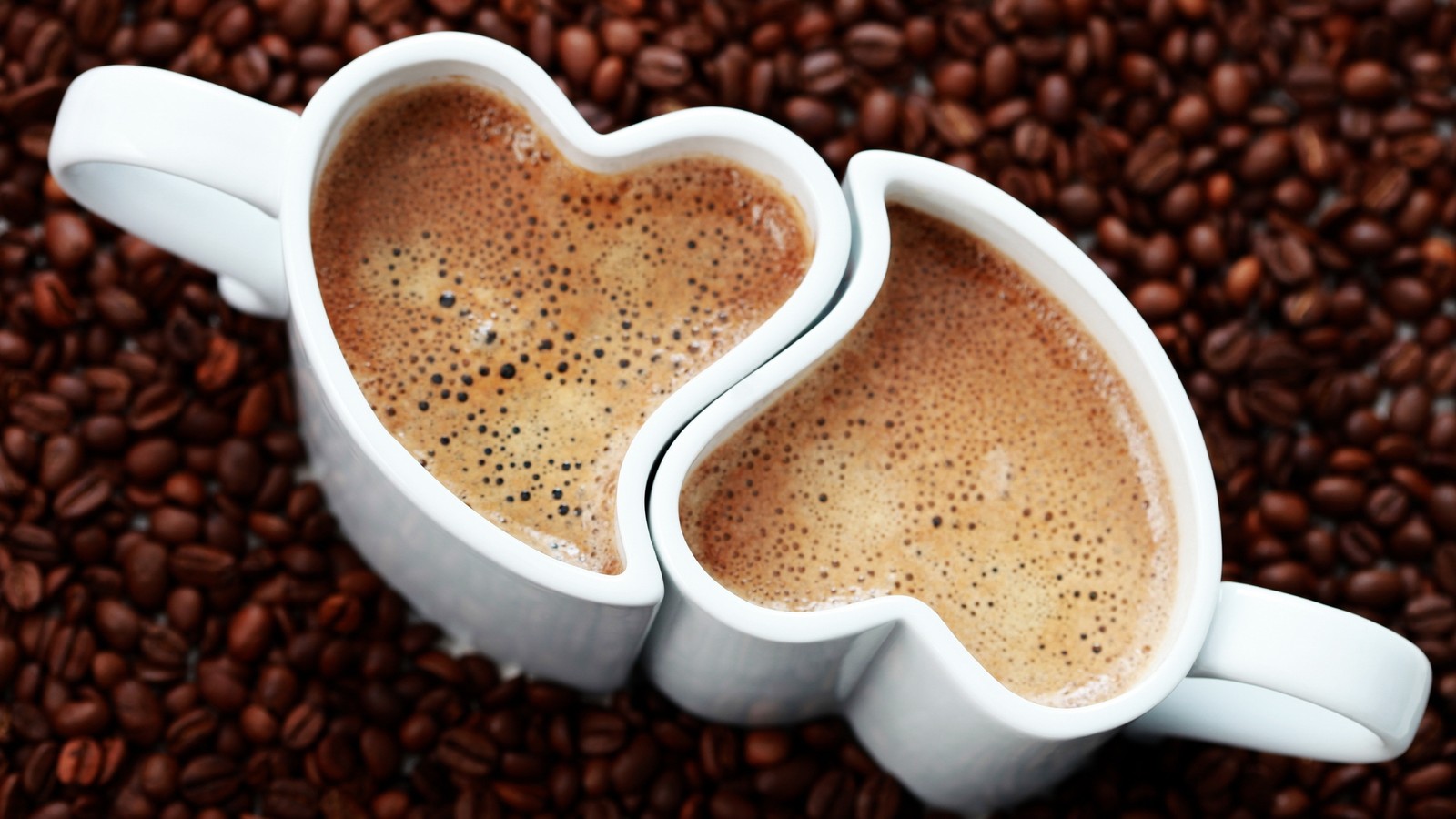 Two cups of coffee with hearts on them on a bed of coffee beans (coffee cup, mug, cup, cafe, caffeine)