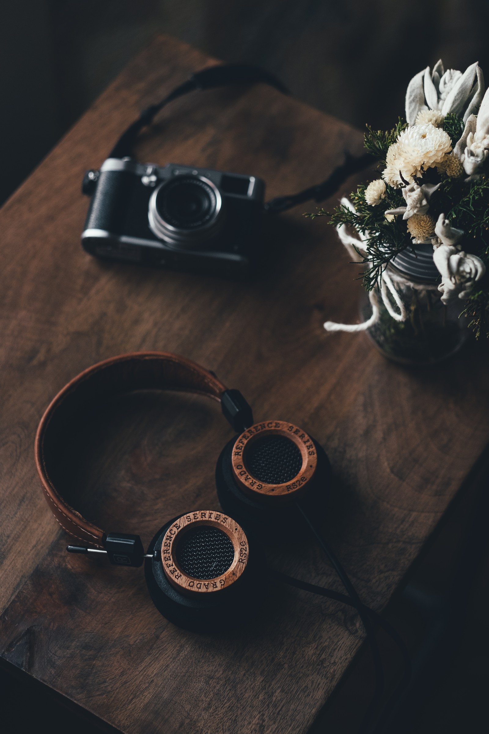 There is a wooden table with a camera and headphones on it (cup, table, tableware, tray, coffee cup)