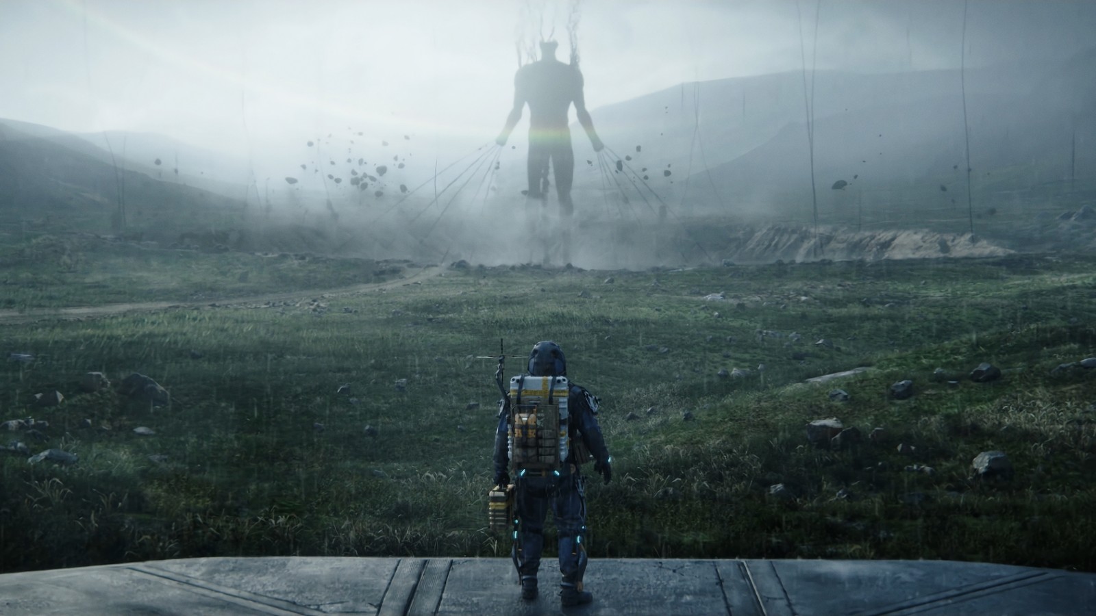 Une image floue d'un homme debout dans un champ avec une statue géante en arrière-plan (death stranding, jeu vidéo)