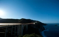 Costa iluminada pela lua com ponte e cabeço à noite