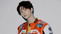 Johnny von NCT 127 in einer stylischen Rennjacke, die eine selbstbewusste Pose vor einem schlichten Hintergrund zeigt.