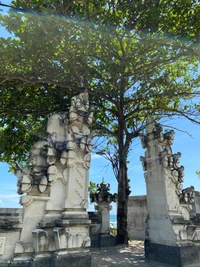 Anciennes sculptures en pierre encadrées par un arbre luxuriant dans un site historique de Bali.