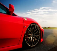 Eleganter roter Ferrari-Supercar mit stilvollen Leichtmetallrädern vor einem malerischen Himmel.