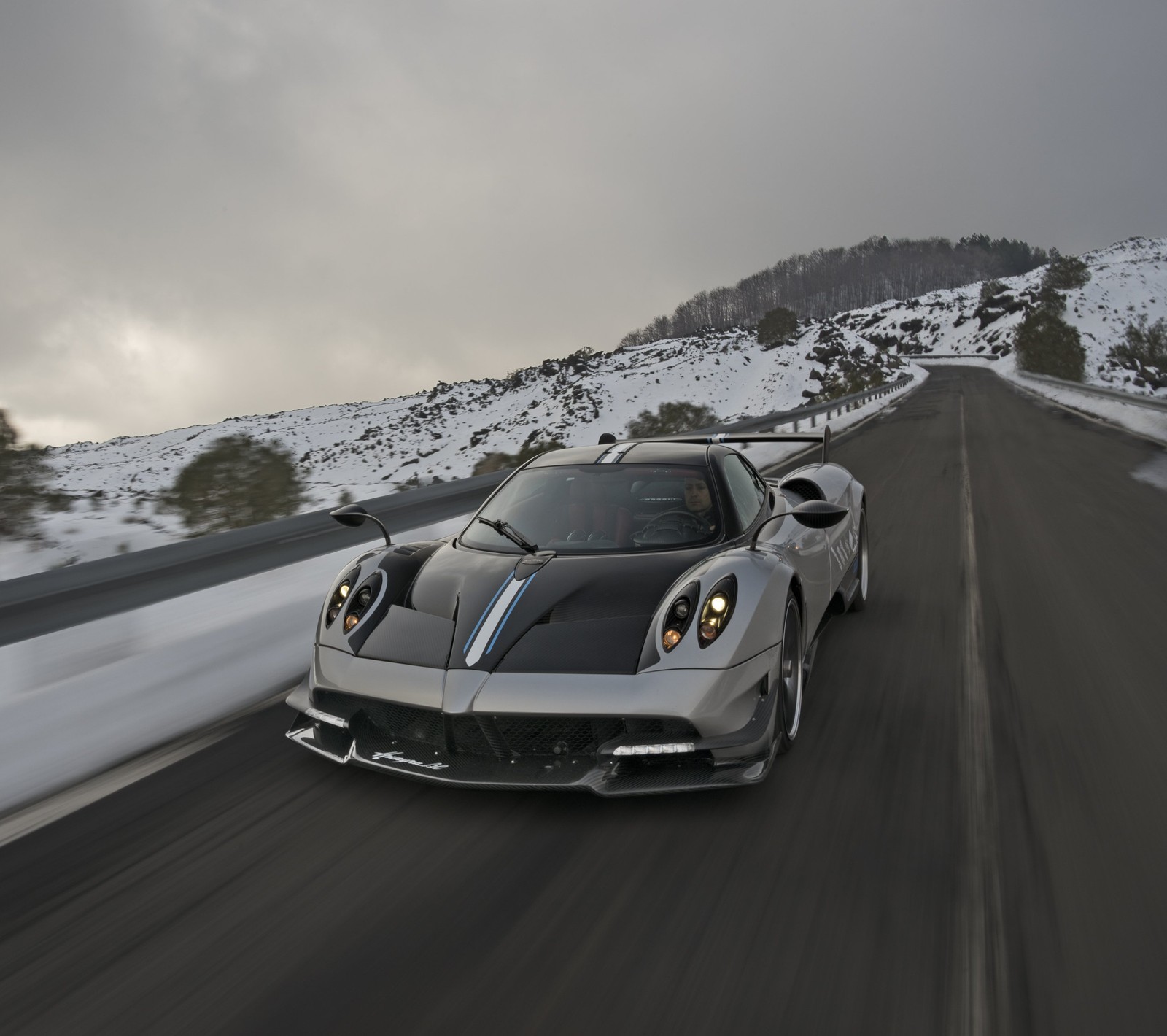 A close up of a silver sports car driving on a snowy road (black, italy, pagani, silver, snow)