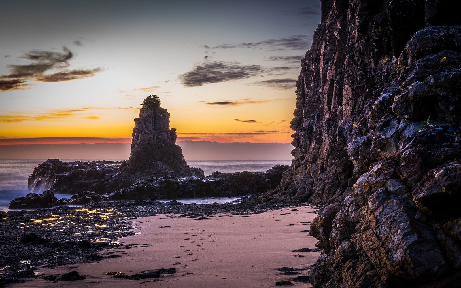 Uma vista de uma praia rochosa com uma formação rochosa ao fundo (rocha, costa, por do sol, mar, praia)