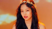 Kim Jennie radiates elegance with a crown and captivating gaze against a warm, vibrant backdrop.