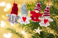 Enfeites de Natal coloridos pendurados em uma árvore de pinheiro, apresentando figuras alegres em trajes festivos contra um fundo quente e cintilante.