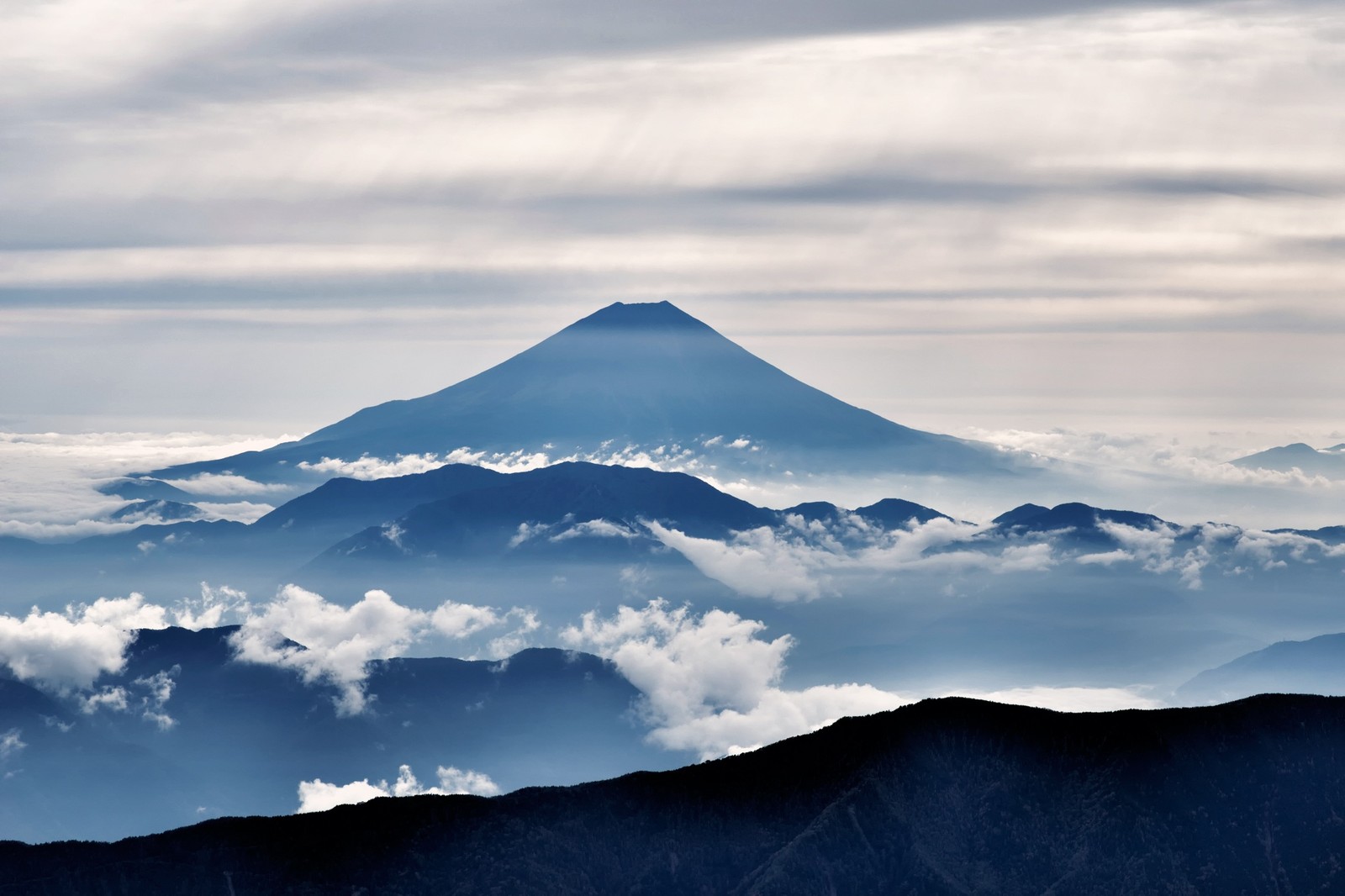 Montagnes avec un grand sommet au loin et des nuages au premier plan (montagne, formes montagneuses, stratovolcan, nuage, chaîne de montagnes)