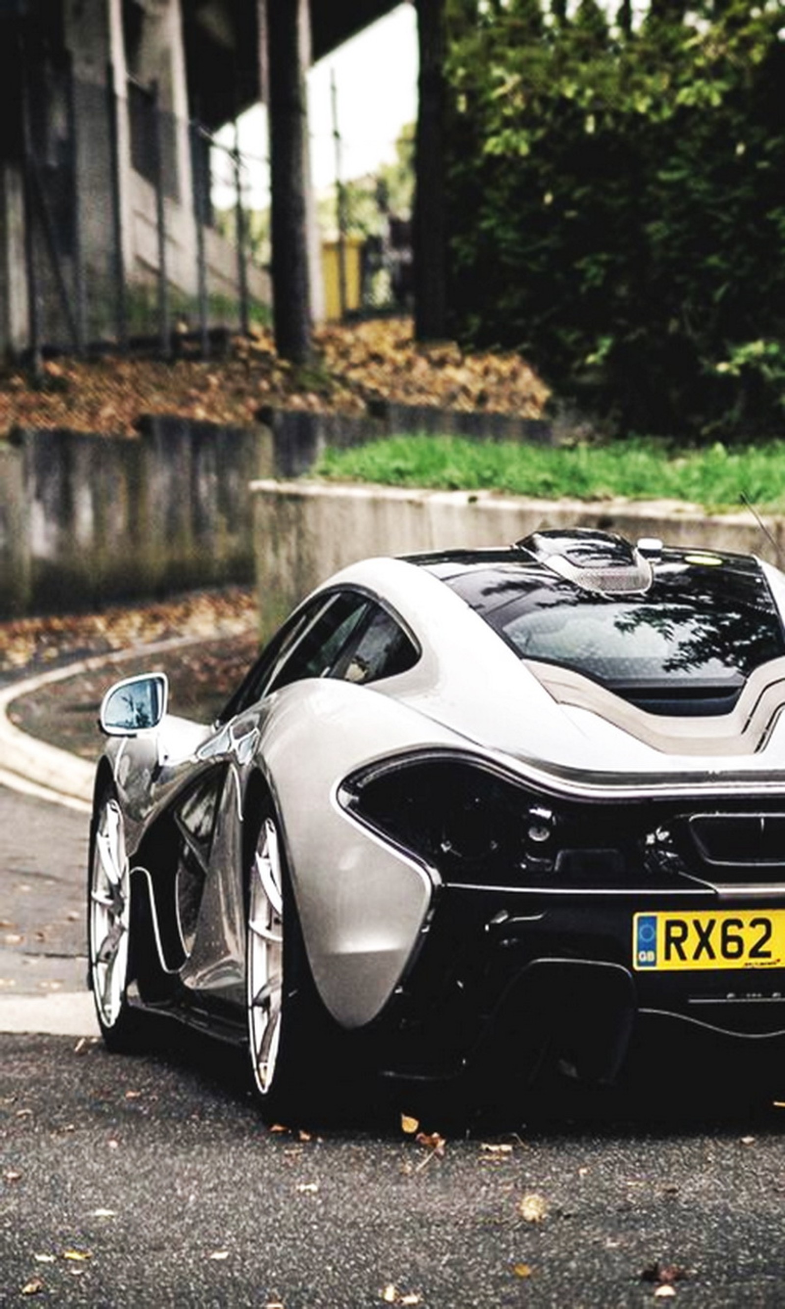 Un primer plano de un coche deportivo plateado estacionado en una calle (coche, mclaren, blanco)