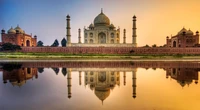 Taj Mahal bei Sonnenaufgang, der seine ikonische Kuppel und die symmetrische Reflexion im ruhigen Pool zeigt, eingerahmt von der Agra Festung.