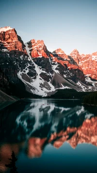 Majestic reflections of snow-capped peaks in the serene waters of Moraine Lake, surrounded by lush forest and dramatic mountain landscapes in Banff National Park.