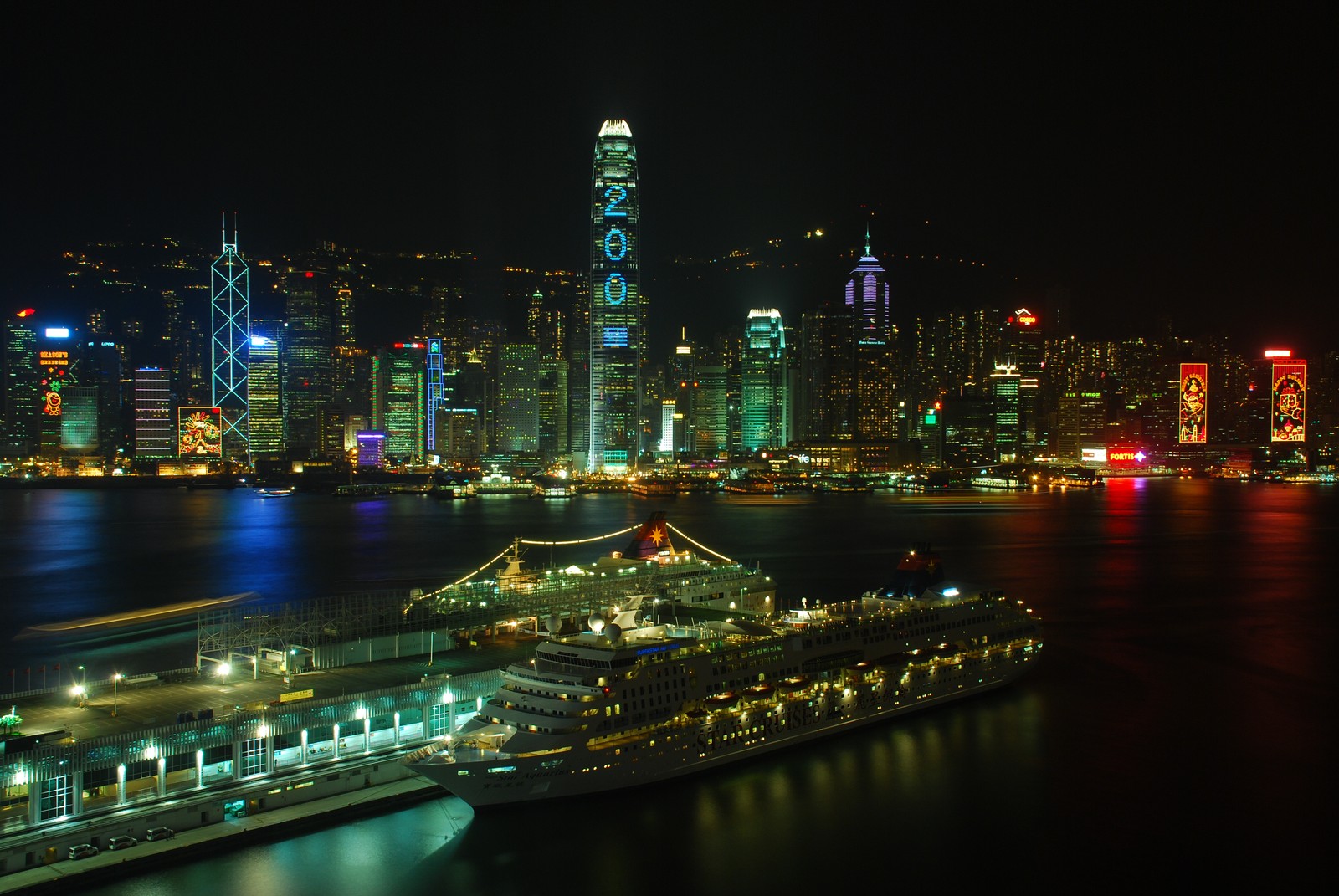 Uma visão aérea de uma cidade à noite com um navio de cruzeiro em primeiro plano (victoria harbour, cidade, paisagem urbana, noite, metrópole)