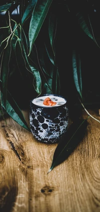 Stylish cup of creamy drink garnished with clementine, set against lush green leaves on a wooden table.