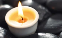 Illuminated Candle Surrounded by Smooth Black Stones