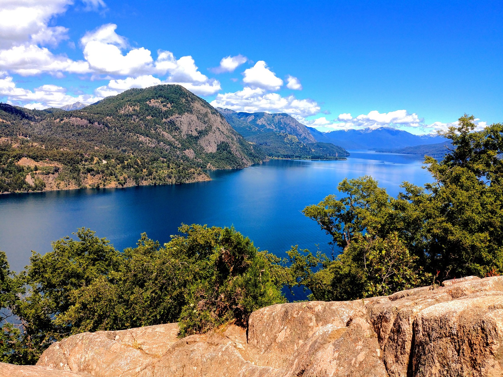 Uma vista de um lago e montanhas de um penhasco (lago, rochas, água, montanha, árvores)