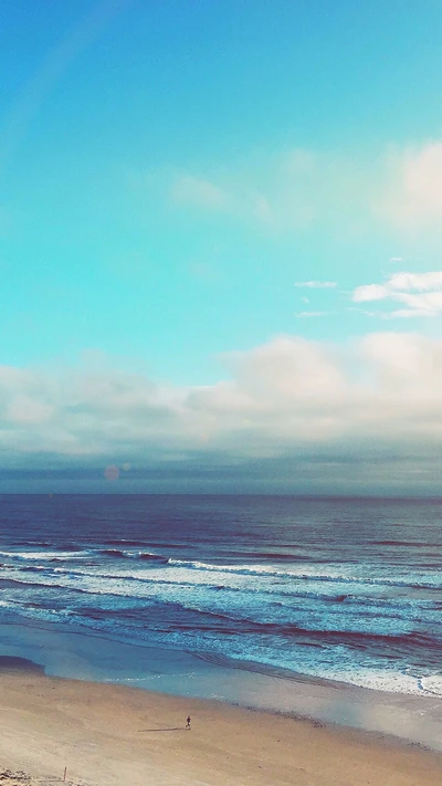 Paisaje de playa tranquilo bajo un cielo azul con nubes y olas del océano