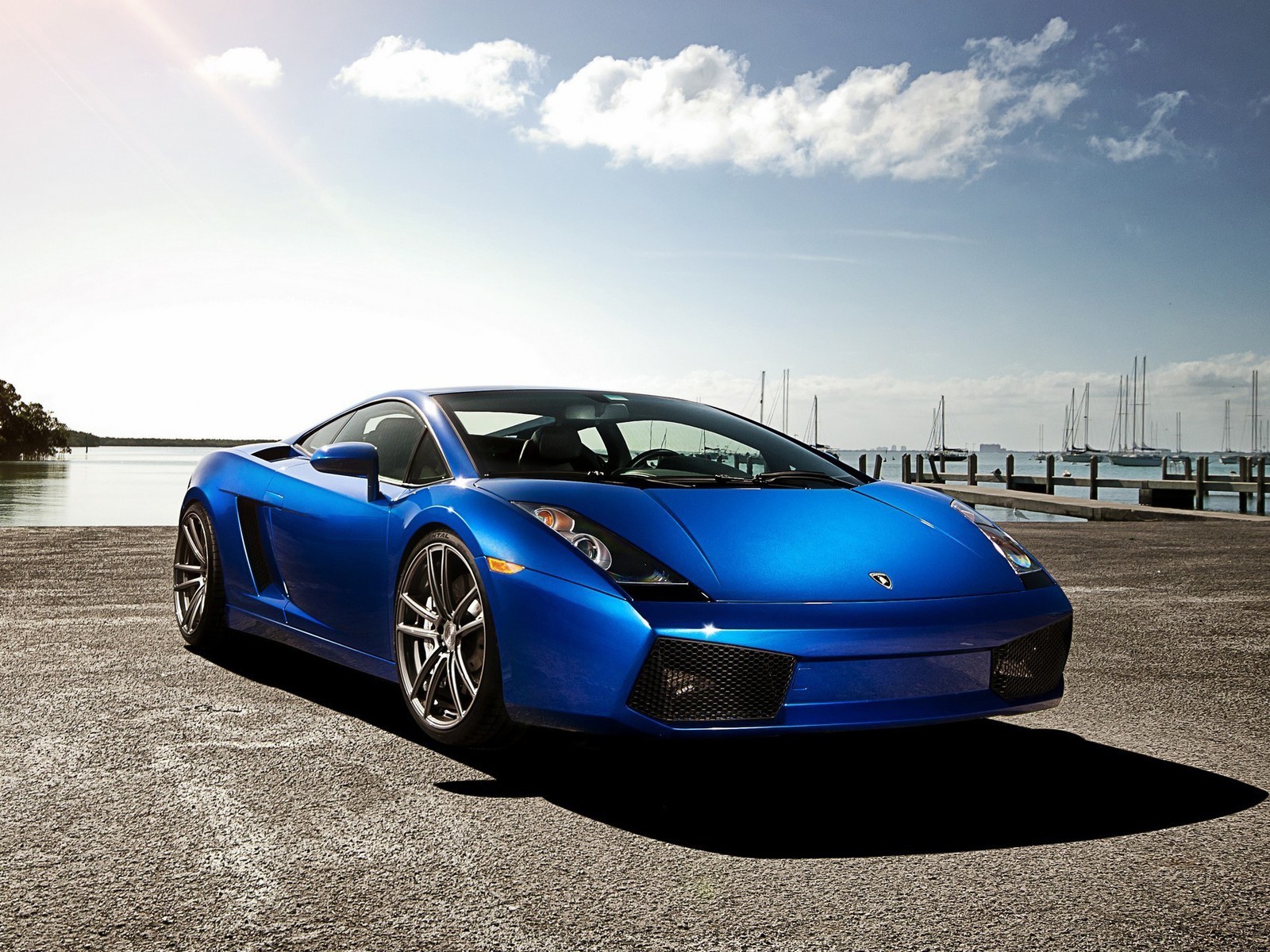 Carro esportivo azul estacionado em um estacionamento perto de um corpo d'água (gallardo, lamborghini)