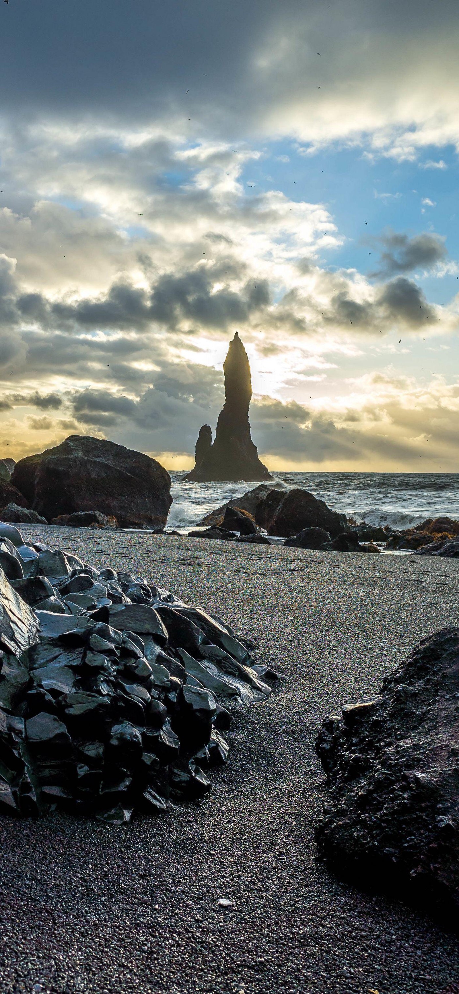 There is a large pile of rocks on the beach near the water (sea, cloud, water, natural landscape, sunlight)