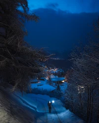 Winter Evening Glow: A Man with a Lantern Illuminates a Snow-Covered Path Under a Blue Sky