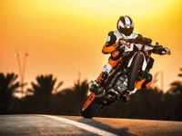 KTM 990 Super Duke realizando un impresionante truco contra un vibrante fondo de atardecer.