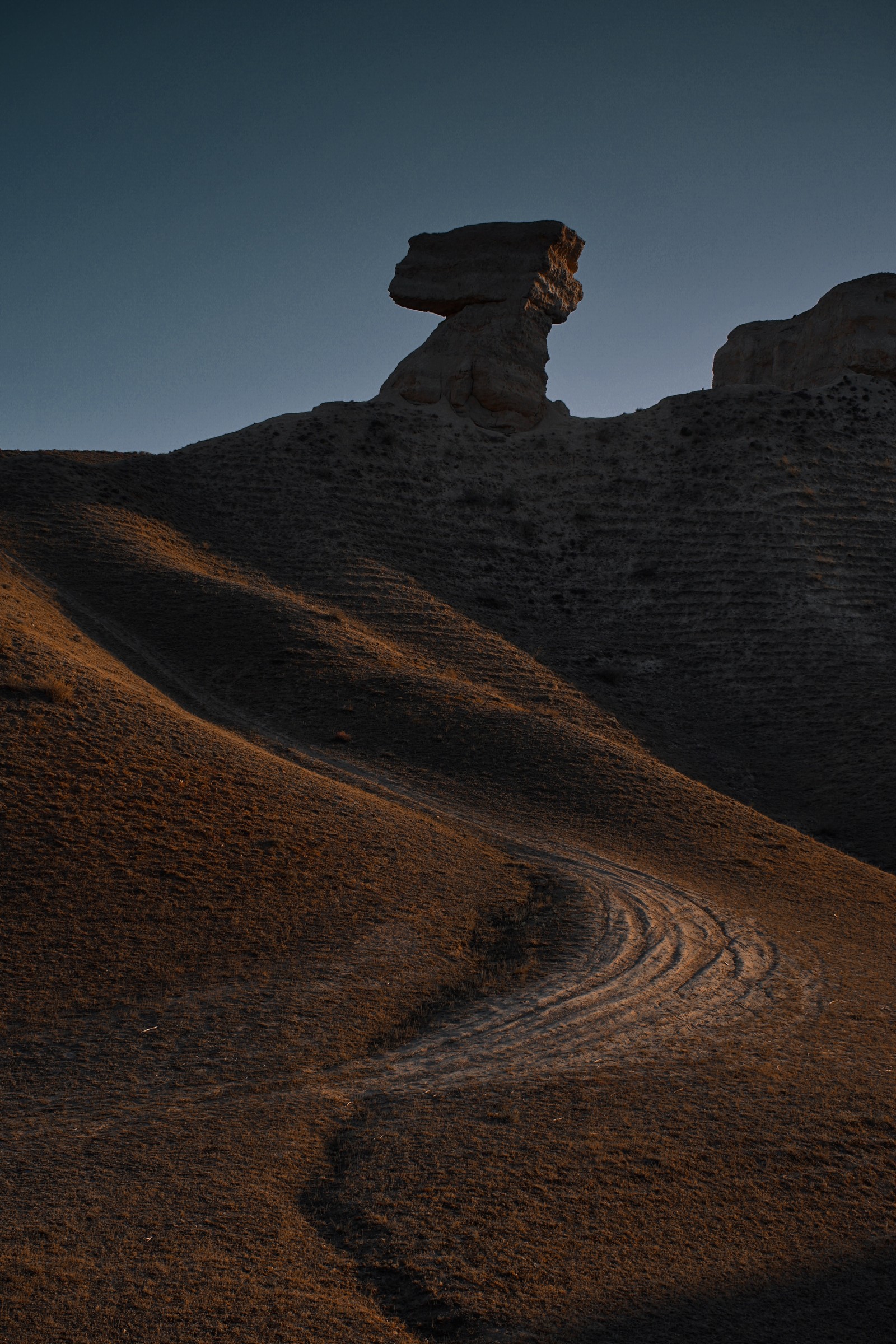 Hay una formación rocosa en una colina con una pequeña ola en primer plano (entorno natural, cielo, marrón, geología, roca)