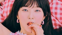 Irene from Red Velvet with striking blue eyes, playfully holding a cherry, surrounded by a pink and red checkered backdrop.