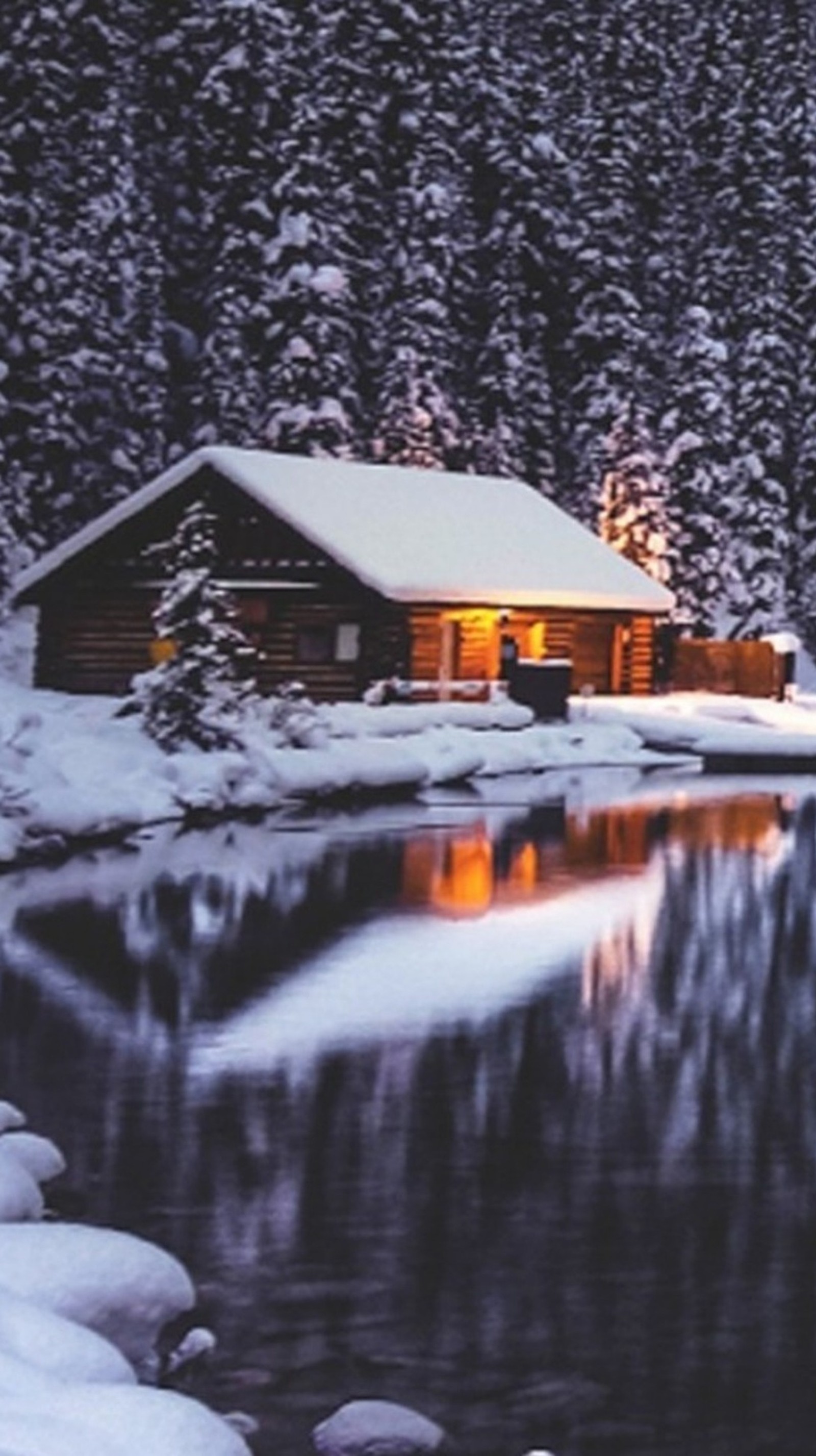 Ein verschneites häuschen am see mit einem beleuchteten baum im hintergrund (haus, see, landschaft, winter)