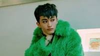 Mark Lee con un vibrante abrigo de piel verde, mostrando un look elegante y juguetón.