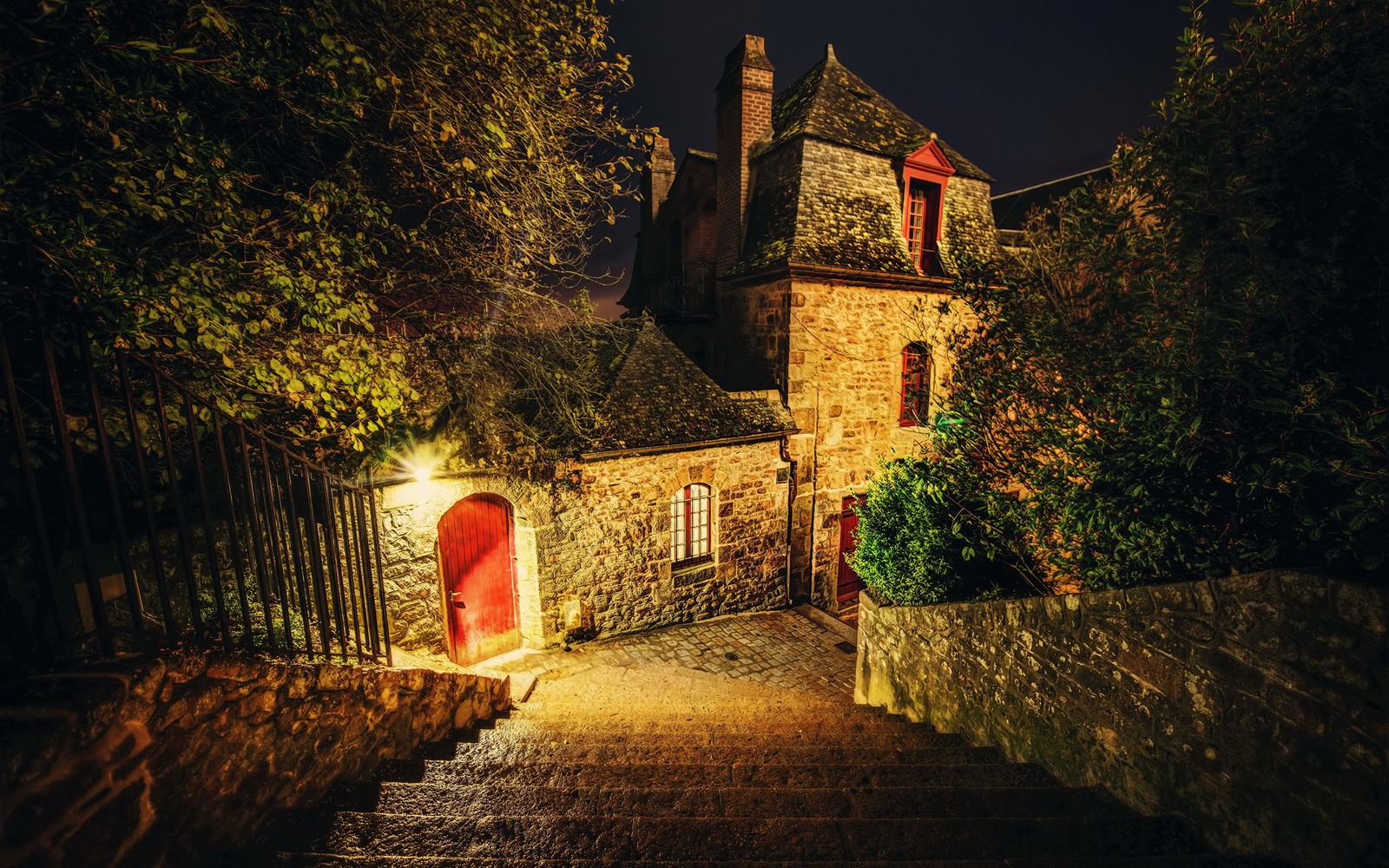 Um close de um edifício de pedra com uma porta vermelha e degraus (noite, iluminação, árvore, caminhada, outono)