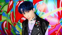 Mark Lee de NCT Dream pose avec confiance devant un fond vibrant et coloré avec des motifs ludiques, mettant en valeur son look élégant et son flair unique.