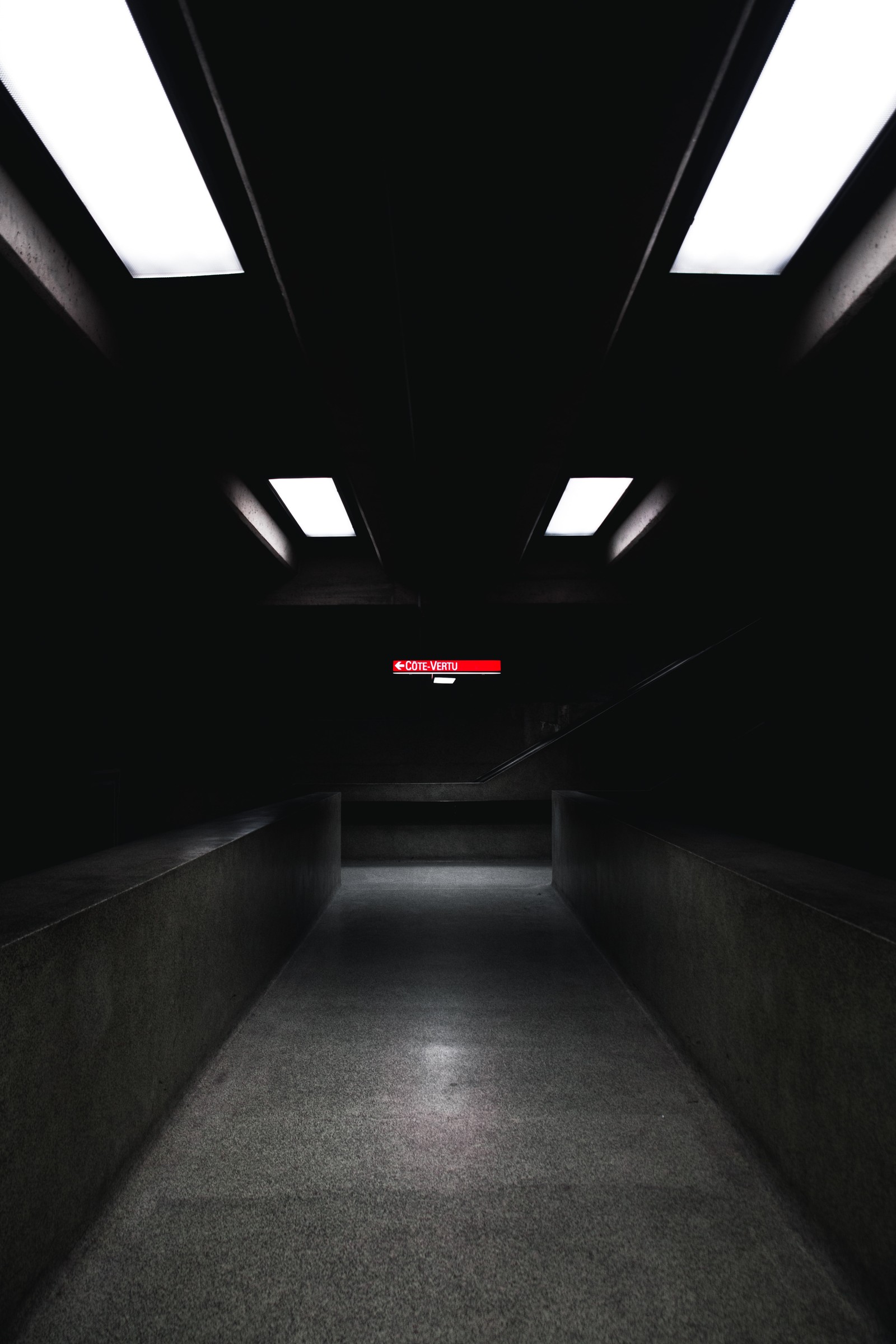 A dimly lit hallway with a red sign in the middle (light, lighting, black, darkness, snapshot)