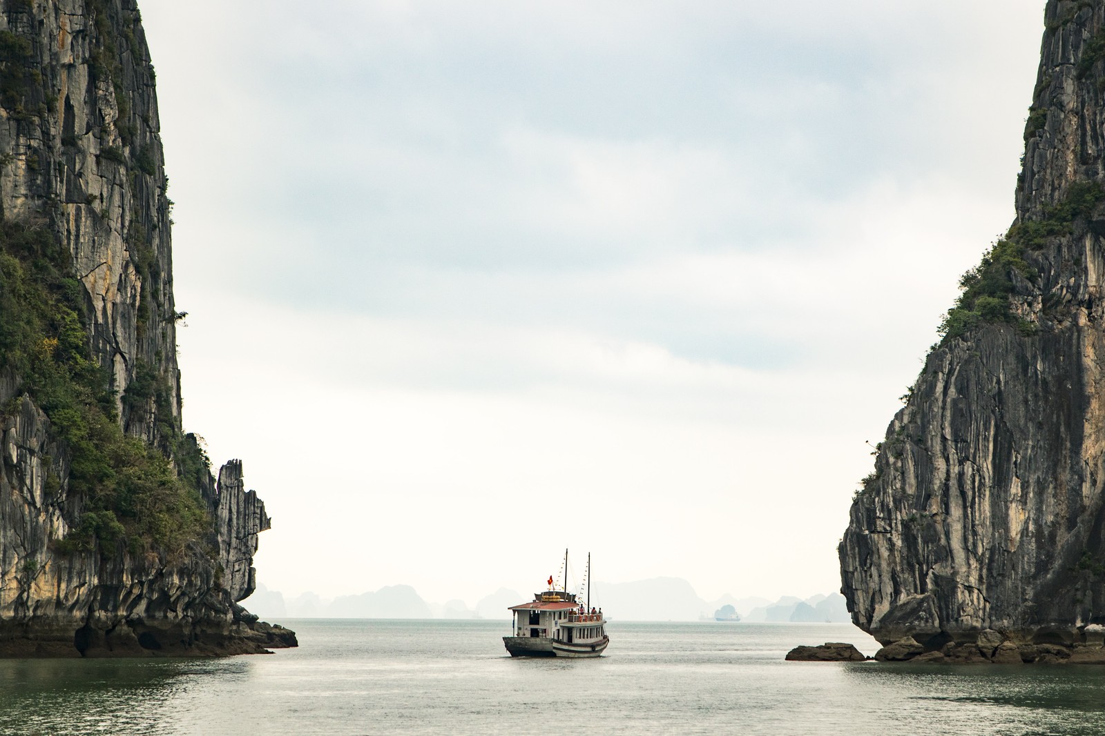 Há um barco flutuando na água perto de algumas pedras (vietnã, vietnam, viagem, férias, turismo)