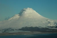 Majestuoso estratovolcán coronado de nieve y nubes, que se eleva sobre un paisaje sereno.