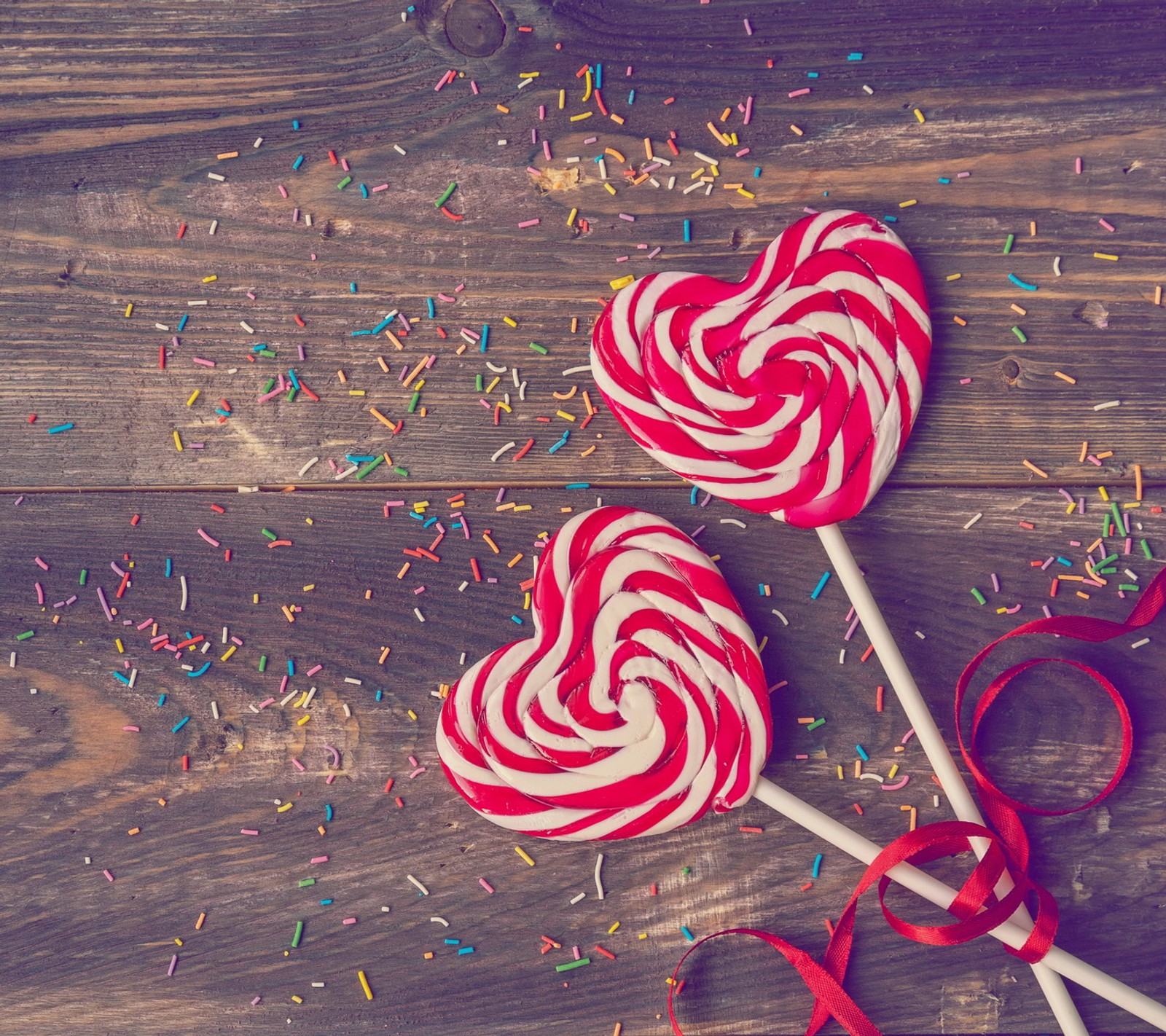 Dos piruletas con rayas rojas y blancas sobre una mesa de madera (corazón, piruleta, amor, romántico)